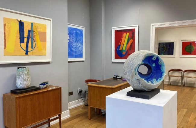 A colour photo of an exhibition of prints with a circular sculpture in the foreground