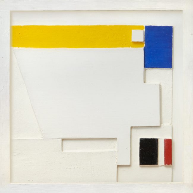 relief of white geometric shapes with areas painted yellow, blue, red and black