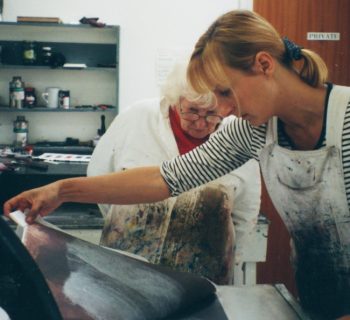 A colour photo of two women looking at an etching being pulled from the etching plate