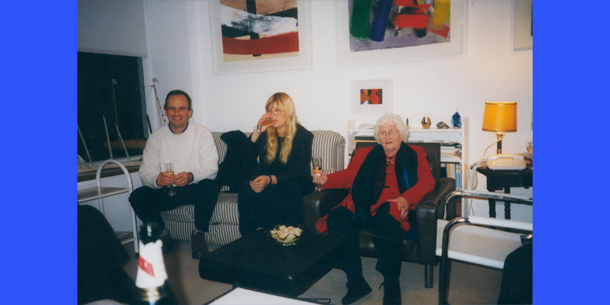 A colour photo of a man and two women seated in a living room drinking champagne